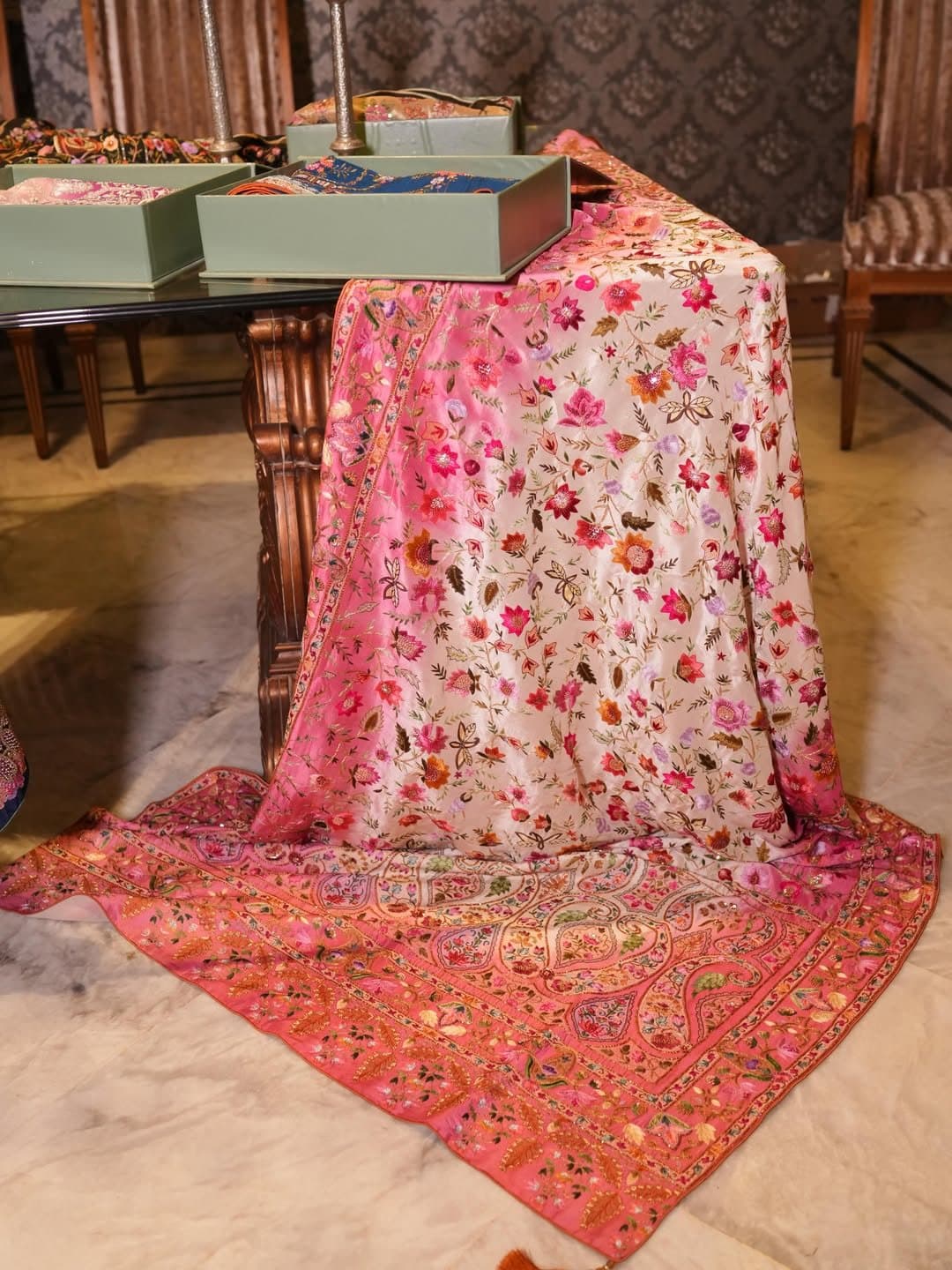 A rose-pink bridal shawl with a densely embroidered floral pallu, spread out on the floor.