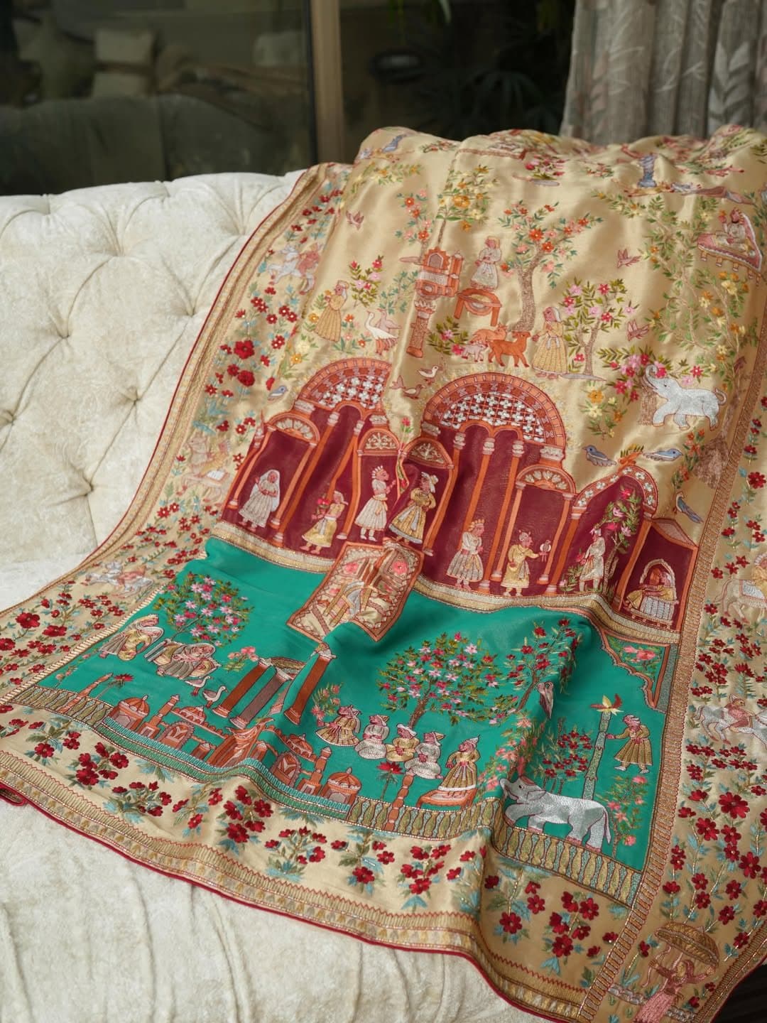 A pictorial kalamkaar shawl showing a court scene in red and emerald, folded over a chair back.
