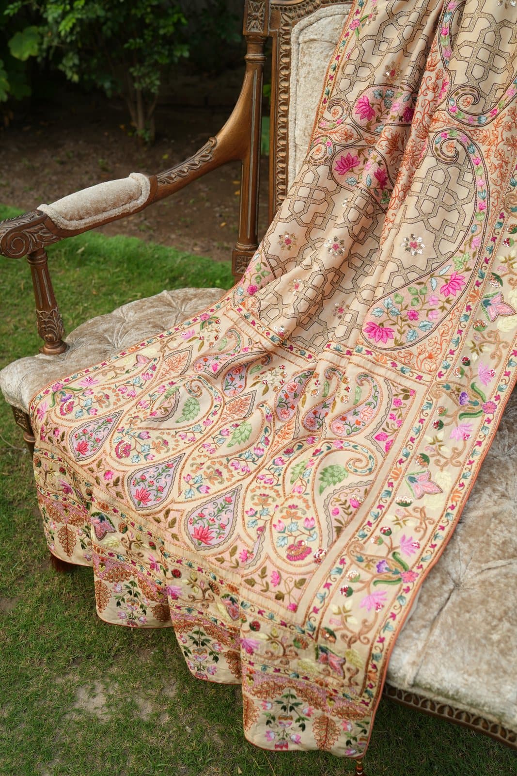 An ivory shawl covered in fine paisley boteh embroidery, spread across an antique settee.
