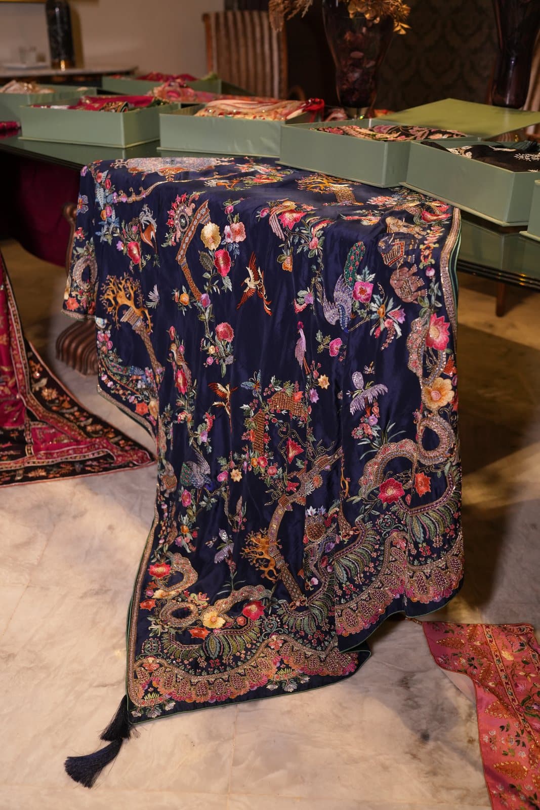 A midnight-blue shawl covered in dense multicoloured floral and bird embroidery, laid over a table.