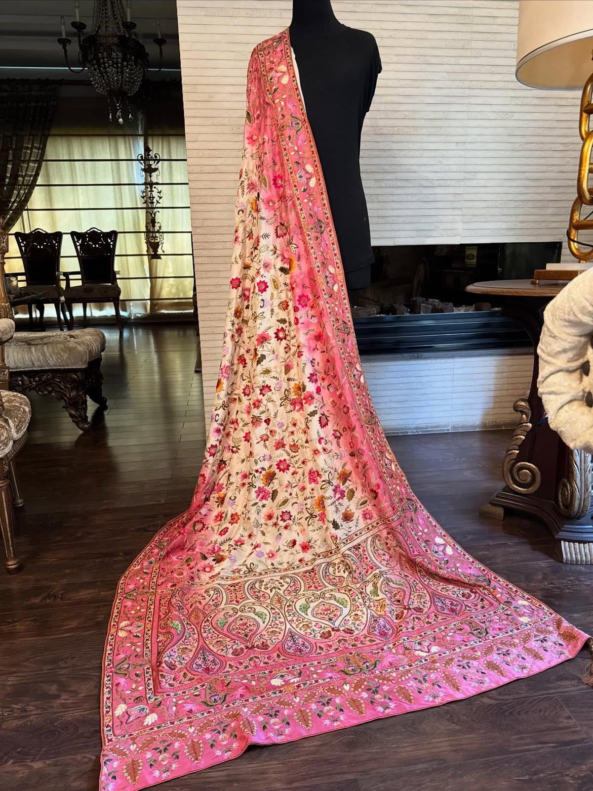 A blush bridal shawl with a wide coral and gold border, arranged in deep folds.