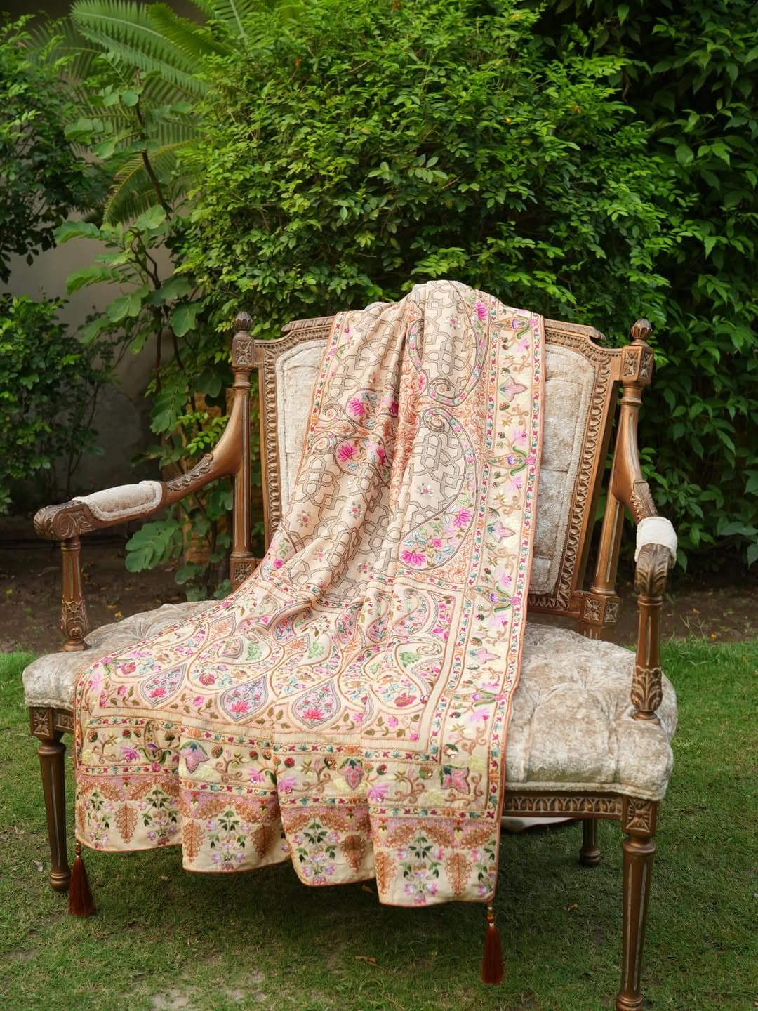 A cream floral shawl spread over a carved antique chair on a lawn.