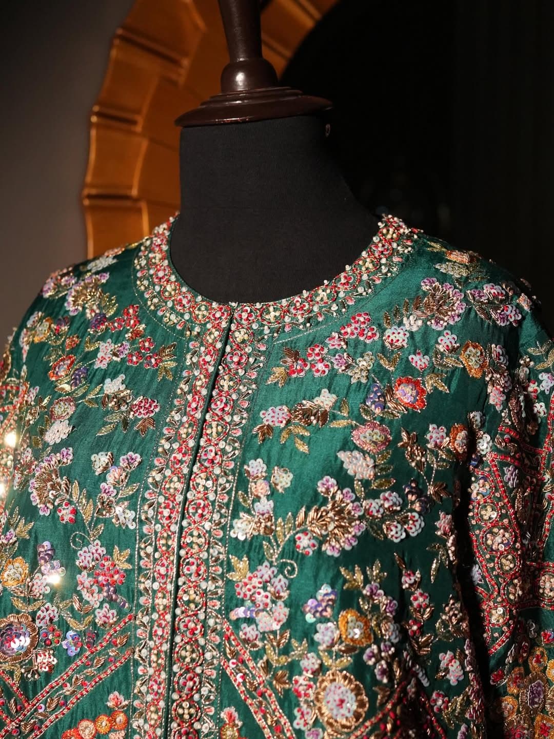 A close view of dense floral embroidery on a dark ground, with metallic thread through the border.