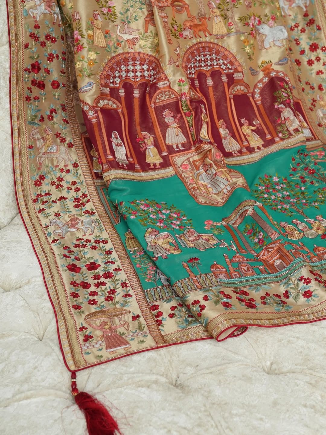 A pictorial shawl in teal and red showing architectural motifs, its border finished with a tassel.