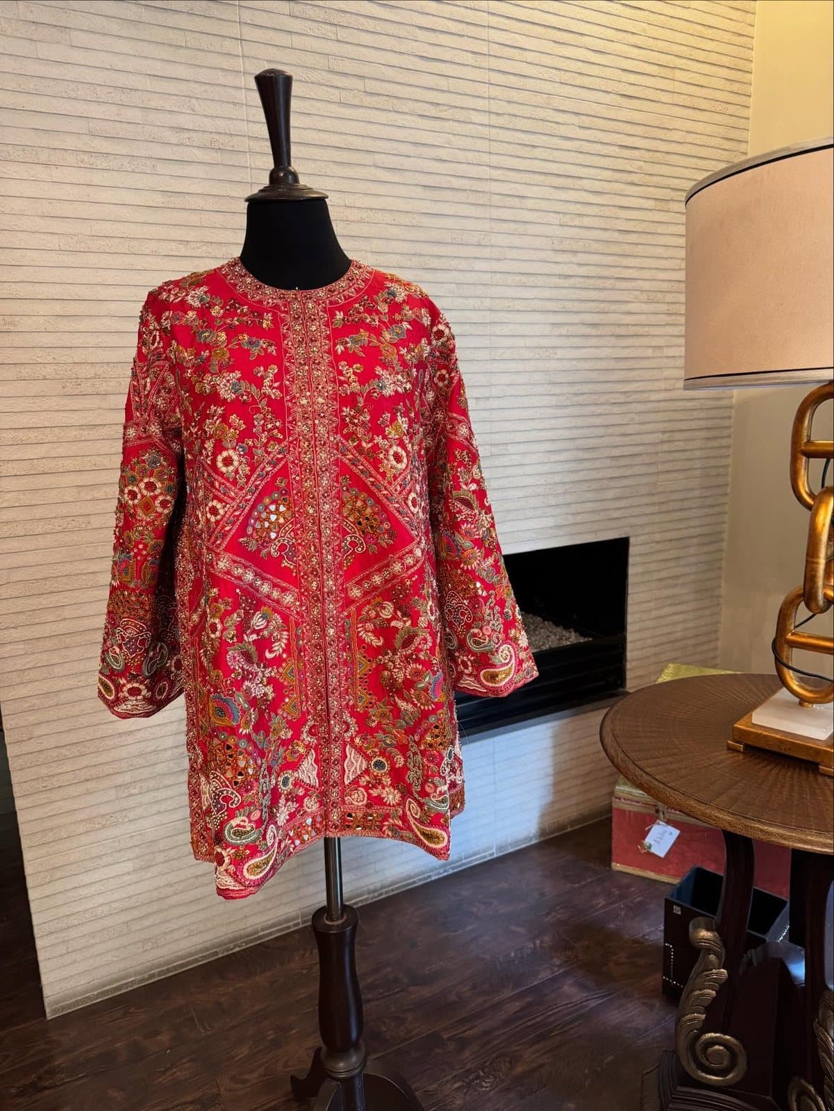 A crimson embroidered jacket on a mannequin in a lamplit room.